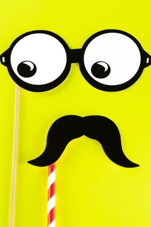 Top view image of funny masks on yellow background. Paper glasses and mustache on bright background. Mens health awareness month. International Mens Day.の写真素材
