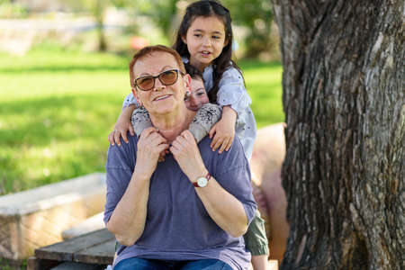 Happy grandma with grandchildren embracing and having fun outdoor on summer sunny day.