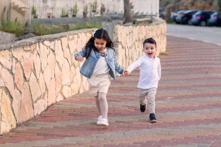 Two cute young preschool children running and playing in a city street. Happy kids run hand in hand. Soft focus and slow shutter speed photography of people in motion to show movement.の写真素材