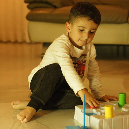 Little funny child sitting on the floor playing a board game in the living room at home.
