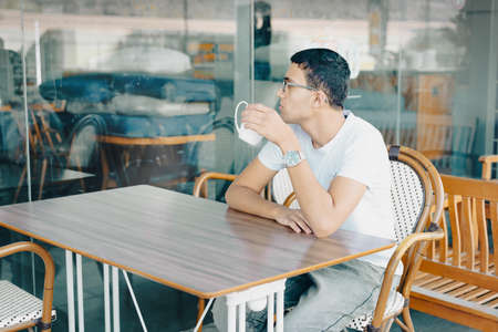 Close-Up Of Young Man Holding Coffe Cup In Cafe. Teenager In A Cafe Drinking Cup Of Tea, Deep In Thought.の写真素材
