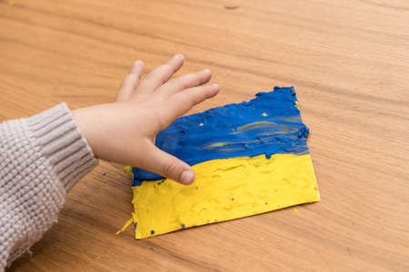 Support for Ukraine. Close up little kid hand makes Ukraine flag out of plasticine. Concept of patriotism, respect, charity, help, and solidarity with the citizens of Ukraine.の写真素材