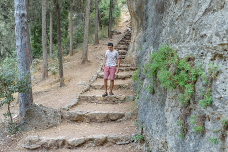 Happy teen walking in woods. A smiling black hair teenager wearing a shorts and t-shirt walking down...