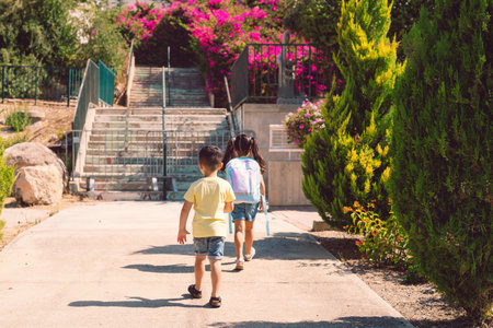 A young children going back to school. Little girl with a tie dye backpack walks to preschool with her brother at a sunny day.の写真素材