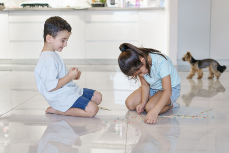 Happy children playing mikado in the fllor of living room at home, close up. Kids spending time...