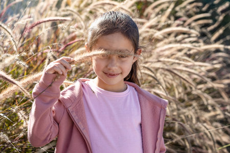 Little girl holding up pampas grass to eyes in front of pampas grass field.の写真素材