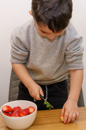 Little child using knife and cut the tops from the strawberries. Selective focus on hands.の写真素材