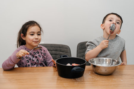 Funny kid licks a spoon with sugar. Portrait joyful children cooking in kitchen.の写真素材