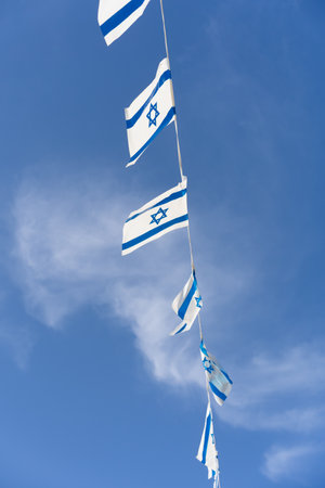 Israeli blue and white flag bunting fluttering against a backdrop of blue sky with white clouds on Independence Day of Israel. Perfect for projects related to Israeli culture and celebrations.の写真素材