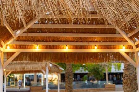 Straw beach umbrella canopy with evening lights and blurred city background. Thatched patio umbrella.の写真素材
