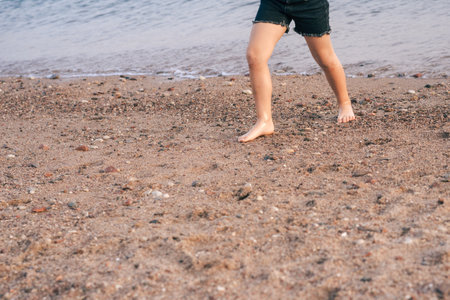 Joyful Little Feet Running Along Pebbled Seashore of the Sea. Carefree Childs Bare Feet Skipping Along the Seashore.の写真素材