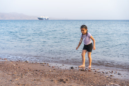 Cute little child playing on the beach. Little beautiful girl with braided hair walking barefoot on the seashore.の写真素材