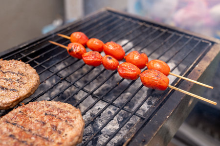 Close-up of a barbecue grill with charred tomato skewers and grilled veggie burgers, showcasing a healthy, antihistamine diet option and trending meat substitutes for modern cuisine.の写真素材