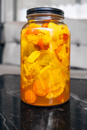 A glass jar filled with a mixture of brightly colored pickled vegetables, including carrots,...