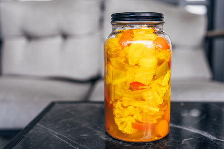 Close-up shot of glass jar filled with vibrant pickled vegetables, including cauliflower, carrots,...