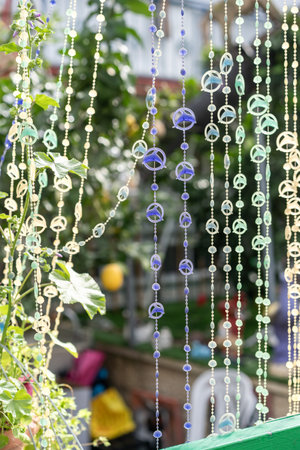 Strings of colorful ornaments hang delicately, swaying in the breeze with a peaceful garden backdrop. The sunlight creates a glowing effect on the translucent decorations.の写真素材