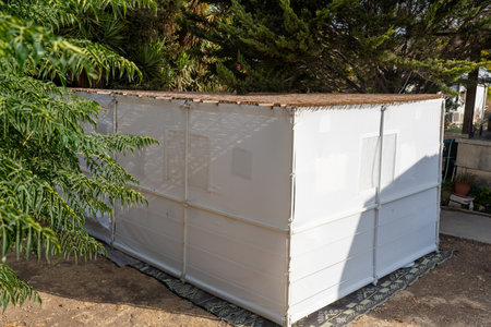 A temporary sukkah stands in a lush backyard, covered with natural materials. The white walls create an inviting space for family and friends during Sukkot festivities.の写真素材