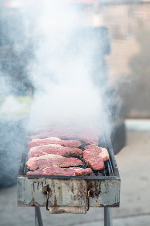 Steaks are being grilled on a metal barbecue, surrounded by billowing smoke. The activity takes place in a backyard setting, perfect for a casual gathering.の写真素材