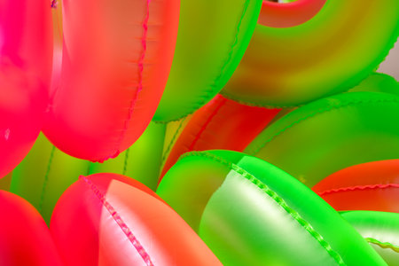 Colorful inflatable swim rings in vibrant pink and green shades are stacked together, perfect for a lively day at the pool or beach party during the sunny summer season.の写真素材