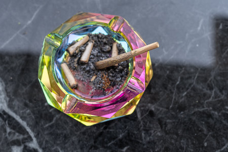 Top view vibrant, multi-colored ashtray sits on a polished marble table, filled with crushed cannabis joints and ash, highlighting a relaxed setting likely frequented by cannabis enthusiasts.の写真素材