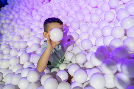 Child playing peek with white balls in a fun indoor pit with purple lights, enjoying playful sensory...