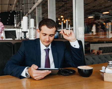 Handsome young businessman smiles and drinks coffee in a cafe. man in a suit with coffee.の写真素材