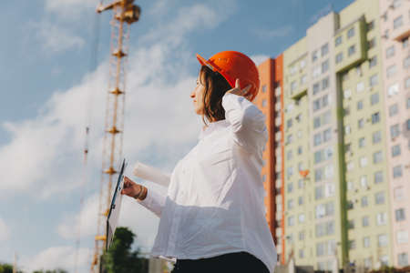 Young beautiful woman architect in white shirt and hard hat holding a flip board. woman in hard hat on a construction site at home.の写真素材