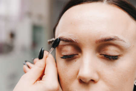 Close-up of a girl's face. The master holds a white pencil and draws the shape of the eyebrows for permanent makeupの写真素材