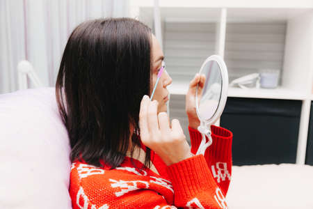 A beautiful girl looks in the mirror and applies makeup. the woman has increased her eyelashes and looks in the mirror.の写真素材