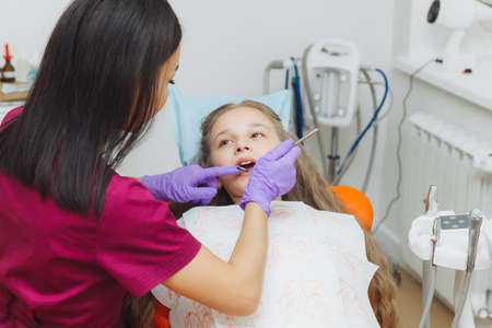 the dentist performs an examination procedure on a cute little girl. Little girl sitting in the dentist's officeの写真素材