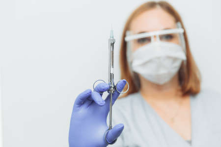 a female doctor or nurse in a medical mask holds a syringe with an injection or medicine. copy space, space for textの写真素材
