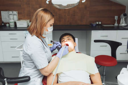 Drilling teeth and sucking saliva with an ejector. dentist treats patient's teeth in modern dental office.の写真素材