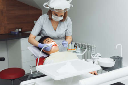 Drilling teeth and sucking saliva with an ejector. dentist treats patient's teeth in modern dental...