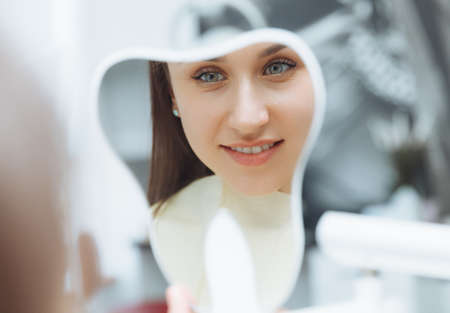 A young woman patient looks at her teeth in the mirror. Modern dental clinic. teeth whitening