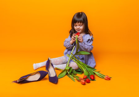 cute little blonde girl with a bouquet of tulips in a cotton dress on a yellow background. March 8の写真素材