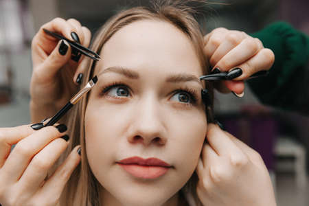 A woman corrects the shape of her eyebrows in a beauty salon. 4 hands do eyebrow correction.