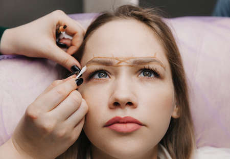 girl with permanent makeup on her eyebrows. The makeup artist makes markings with a brown pencil for eyebrow tattooing.の写真素材