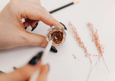 close-up of the master's hands holding a brush with which he stirs the eyebrow paint in a cupの写真素材