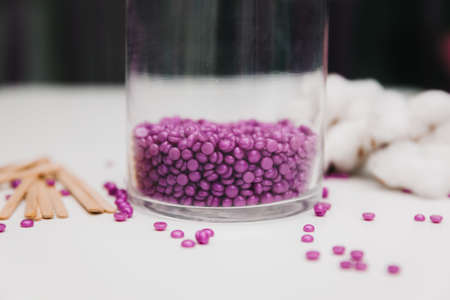 Close-up of purple wax granules scattered from a jar. Beauty procedure to remove unwanted hair from the body.の写真素材