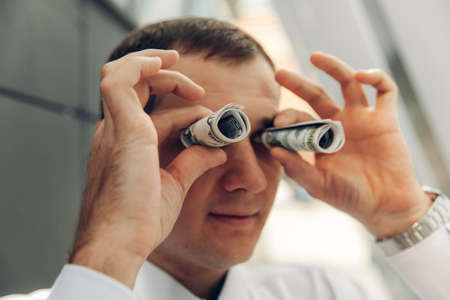 man using money like binoculars. the man twisted the money with a straw near his eyes.の写真素材