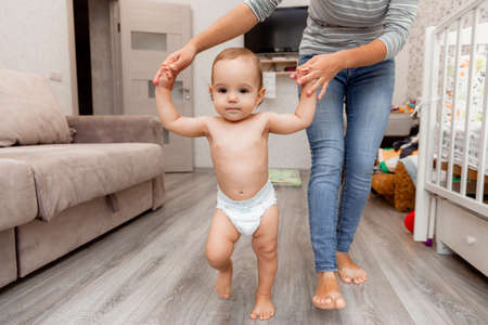 mom helps her child to go. the first steps. the child learns to walk. baby is 11 months old.の写真素材