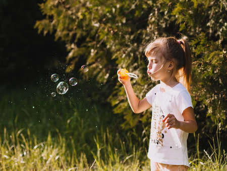 Portrait of a cute little girl blowing soap bubbles in the park in summer.の写真素材