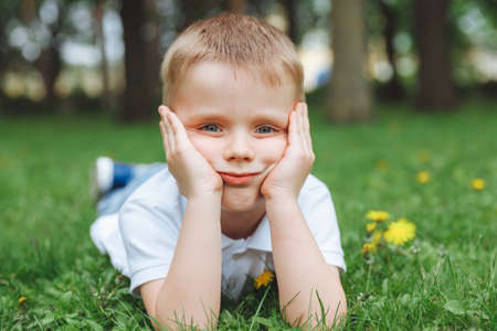 Handsome blond kid, cute boy, lying in the grass in a flower field with dandelionsの写真素材