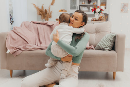 A beautiful young mother is sitting on the living room floor and hugging her little baby. A happy family.の写真素材