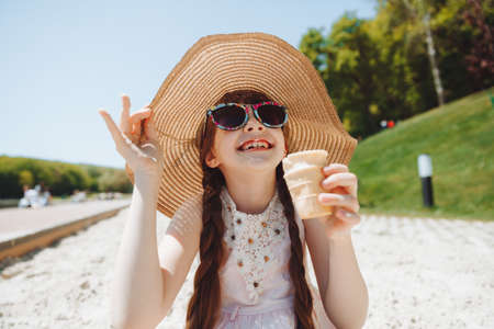 Charming little girl in a hat eats ice cream on the beach of the beach. Summer vacation concept.の写真素材