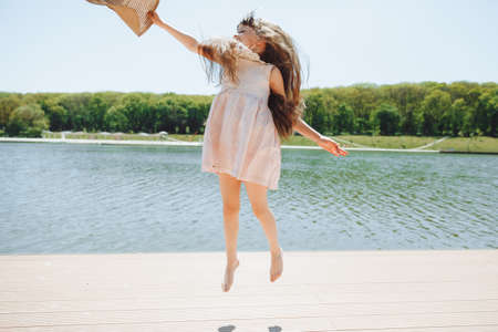 A cute little girl is standing on the pier looking at the beautiful lake. child jumping and having fun on the beachの写真素材