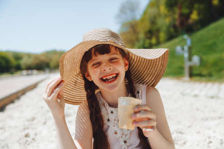Charming little girl in a hat eats ice cream on the beach of the beach. Summer vacation concept.