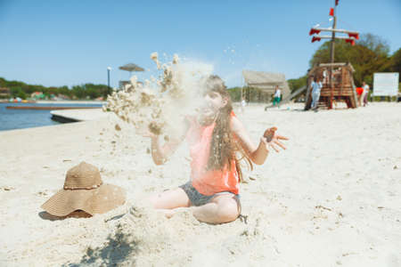A 7-year-old girl plays in the sand on a city beach. vacation and rest. Playful active child on the beach in summer vacationの写真素材
