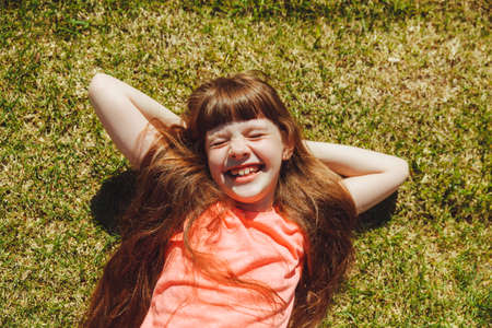 Top view of a happy girl, smiling and lying on the green grass on a summer day in the park