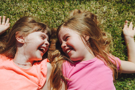 two little beautiful girls lie on the green grass in the summer park, top viewの写真素材